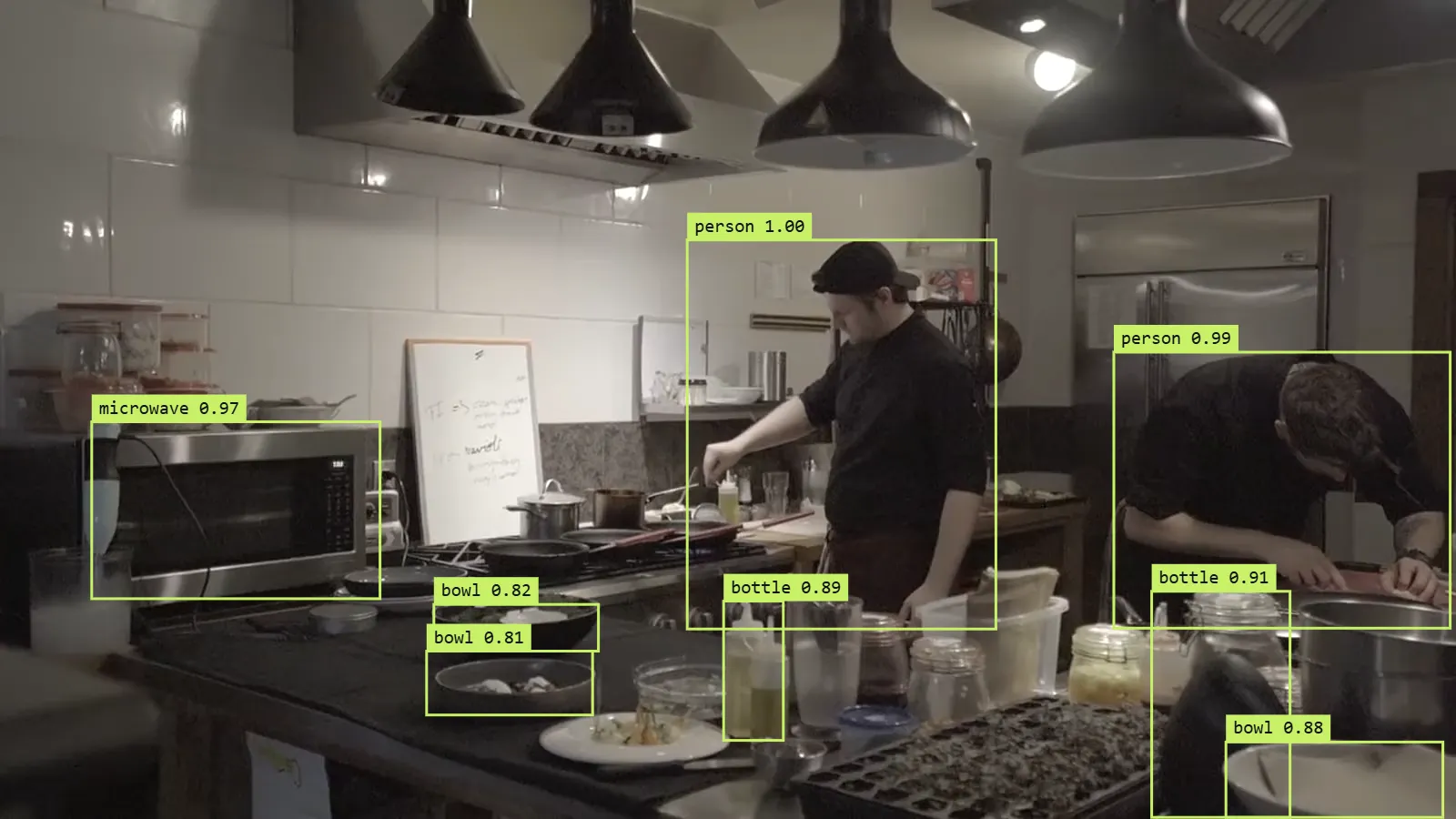 Fotograma de una cocina con las cajas del detector: dos personas, un microondas, botellas y cuencos